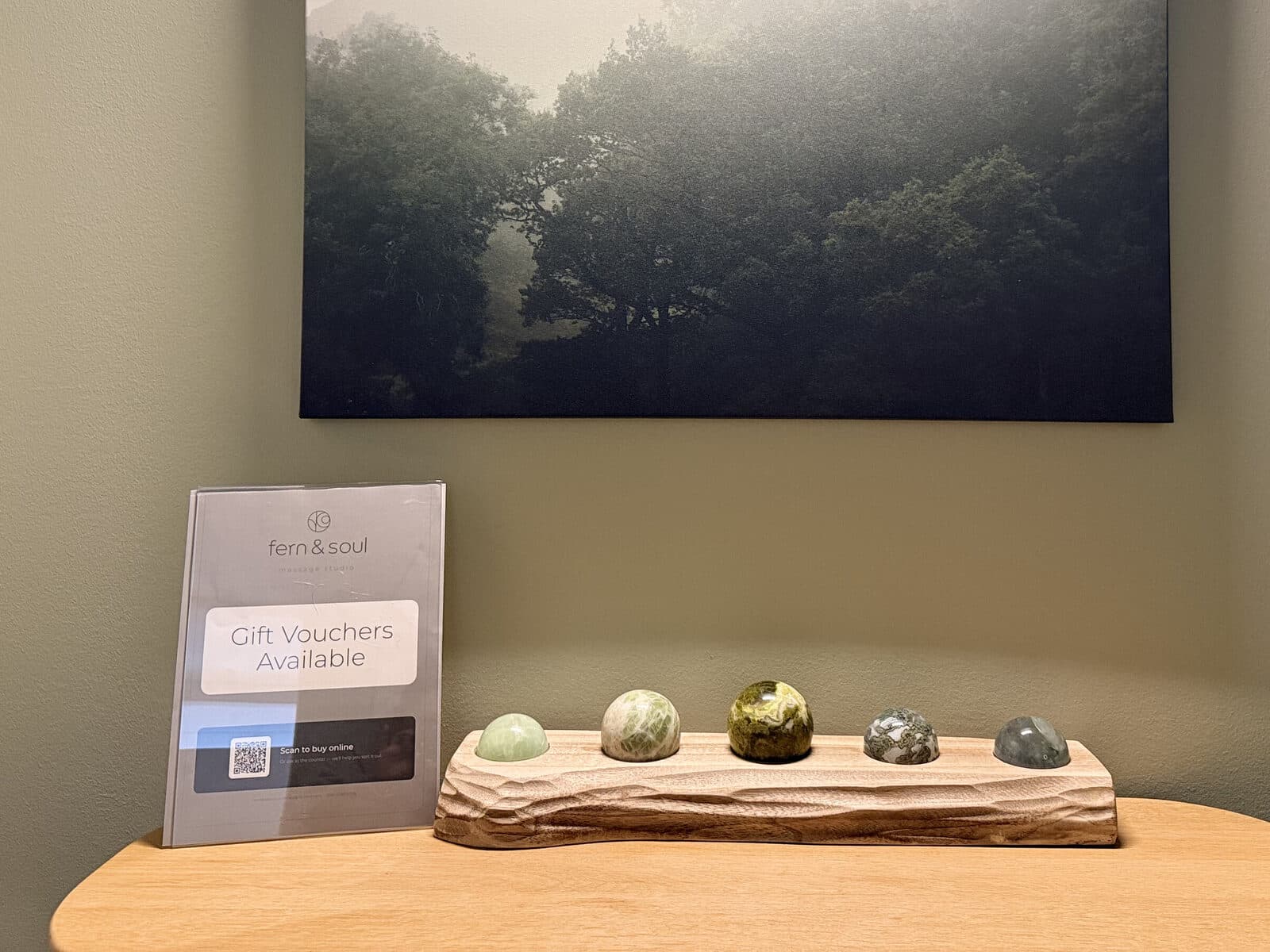 Gift vouchers available sign on the counter at Fern & Soul massage studio Innaloo beside polished stones and a forest canvas