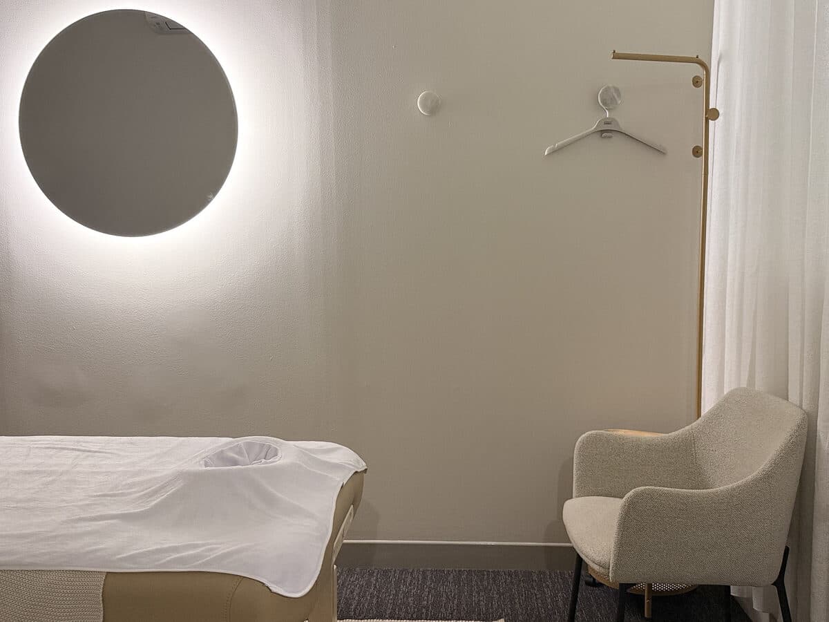 Backlit round mirror and armchair in a calm Fern & Soul massage treatment room in Innaloo