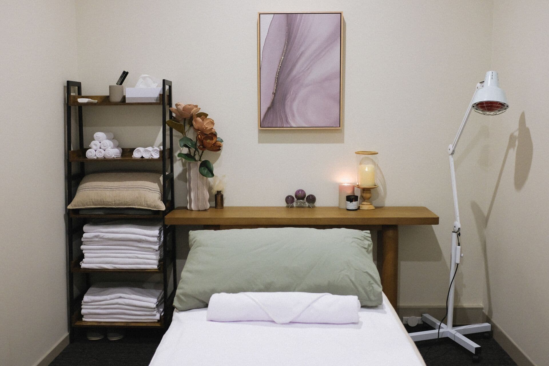Remedial massage table at Fern & Soul in Innaloo, Perth, made up with a sage pillow beside a lit candle and an infrared heat lamp.