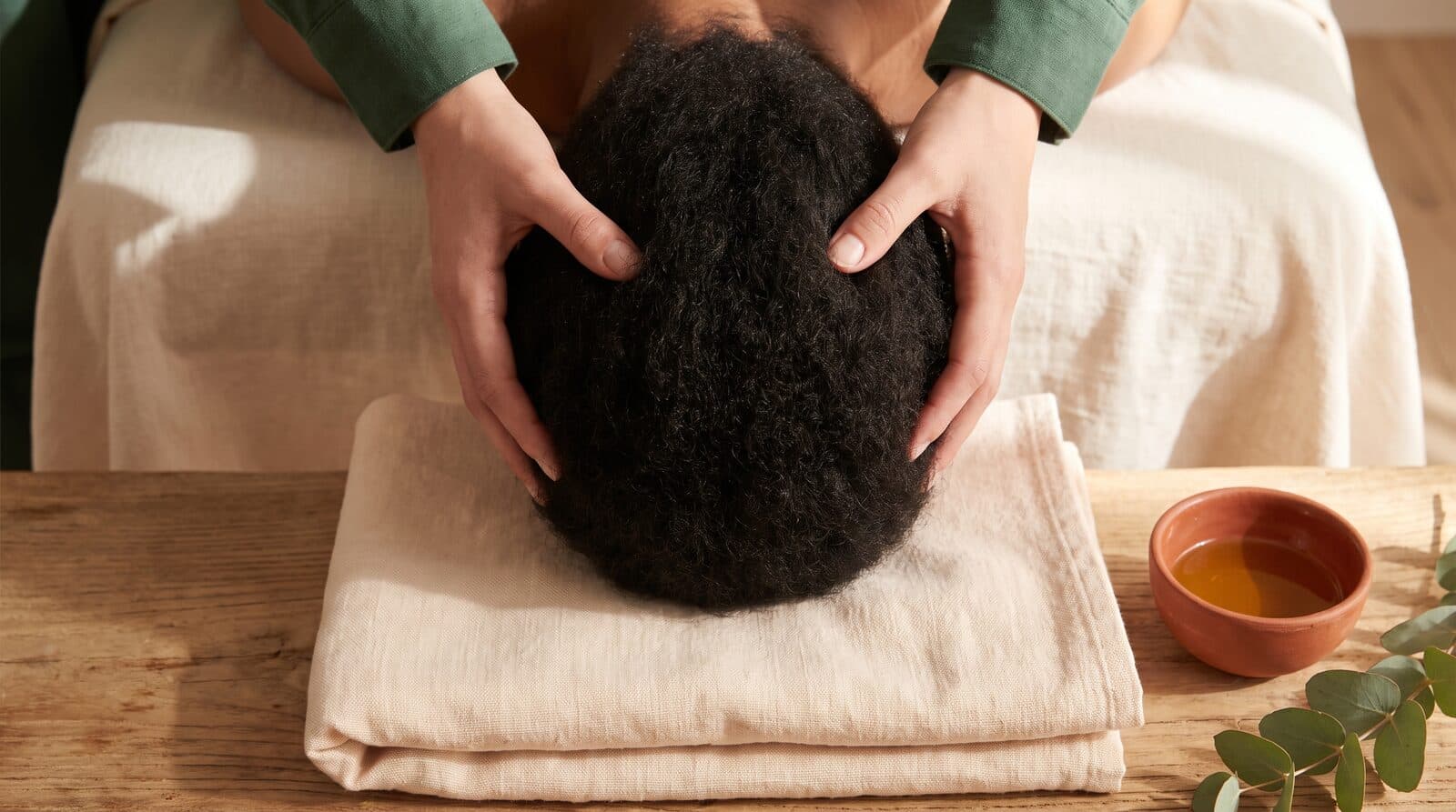 Fern & Soul facial and head massage in Innaloo, a therapist's hands cradling a client's head on a folded cream linen towel.