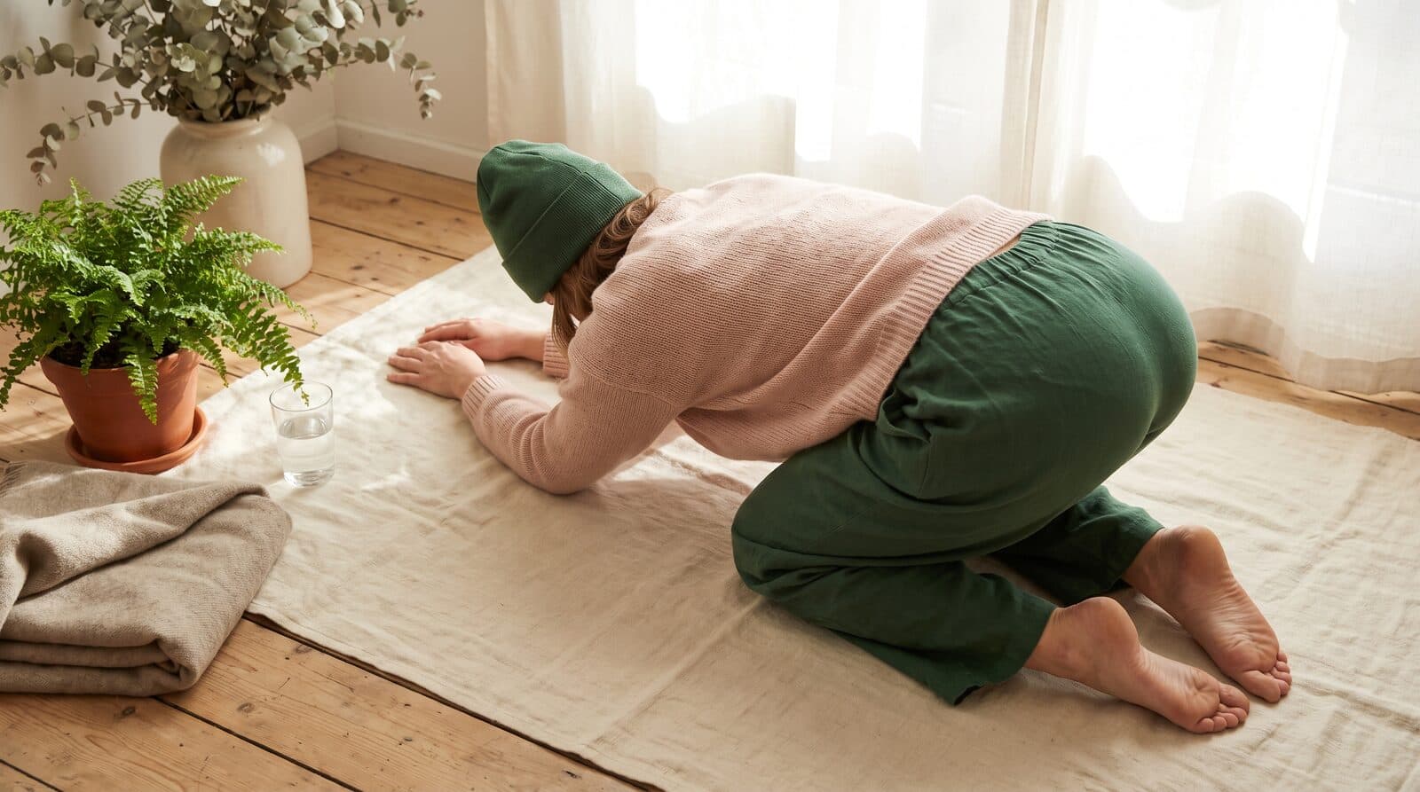 Fern & Soul stretching at home in Innaloo, a person kneeling forward into a gentle stretch on a cream linen mat by a window.