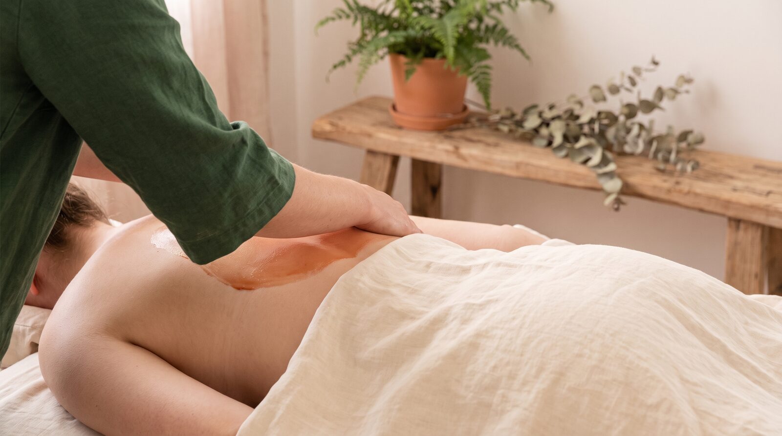 Fern & Soul deep tissue massage in Innaloo, a therapist's forearm working slowly across a relaxed client's shoulder on cream linen.