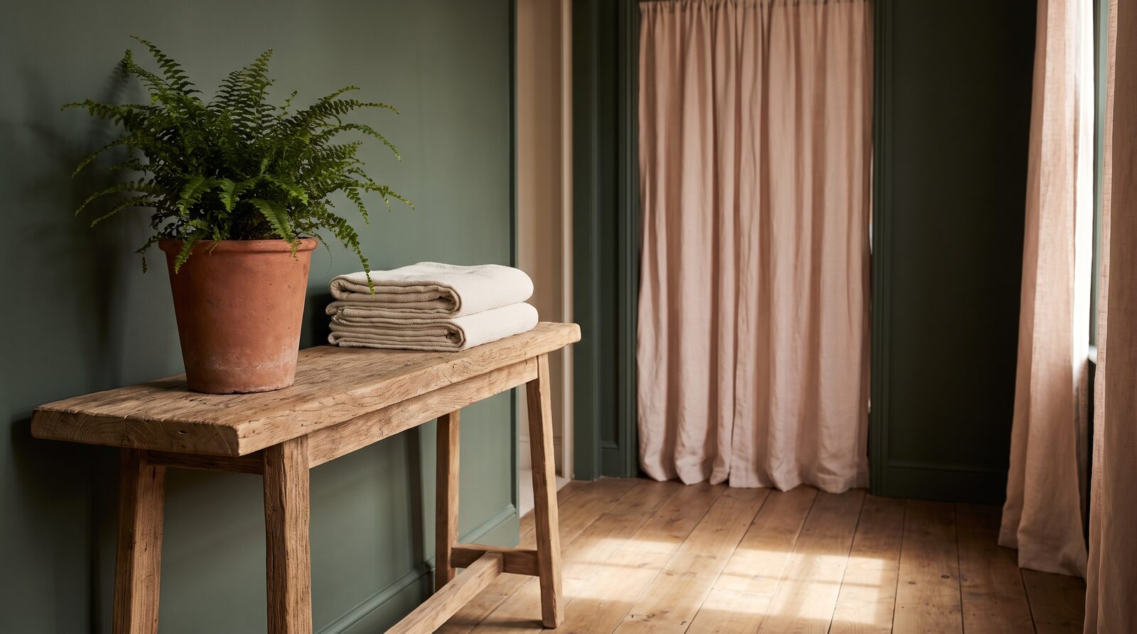 Fern & Soul massage studio entry in Innaloo, a timber console with a potted fern and folded cream towels by a linen curtain.