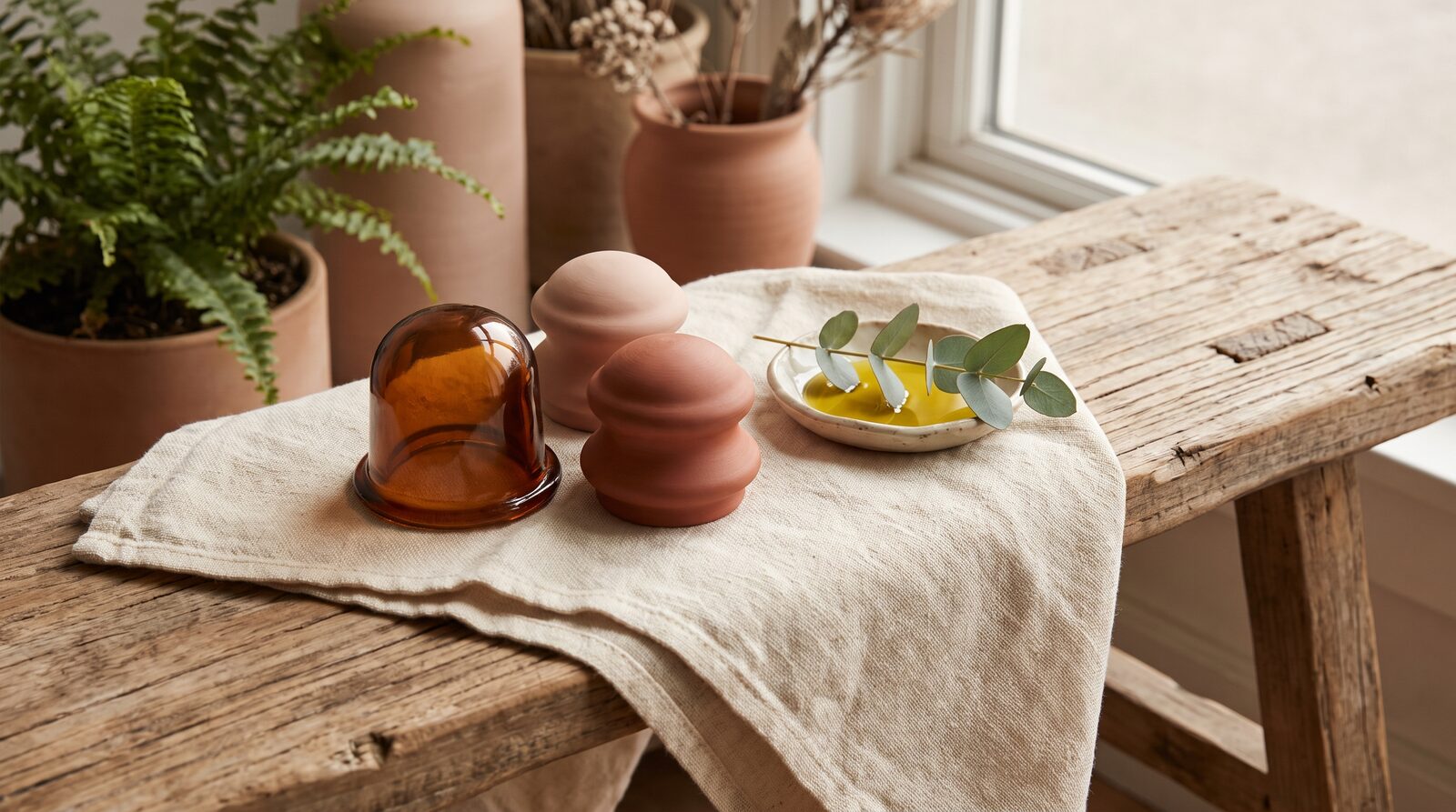 Fern & Soul myofascial cupping set in Innaloo, amber and terracotta massage cups on folded cream linen with a dish of oil.