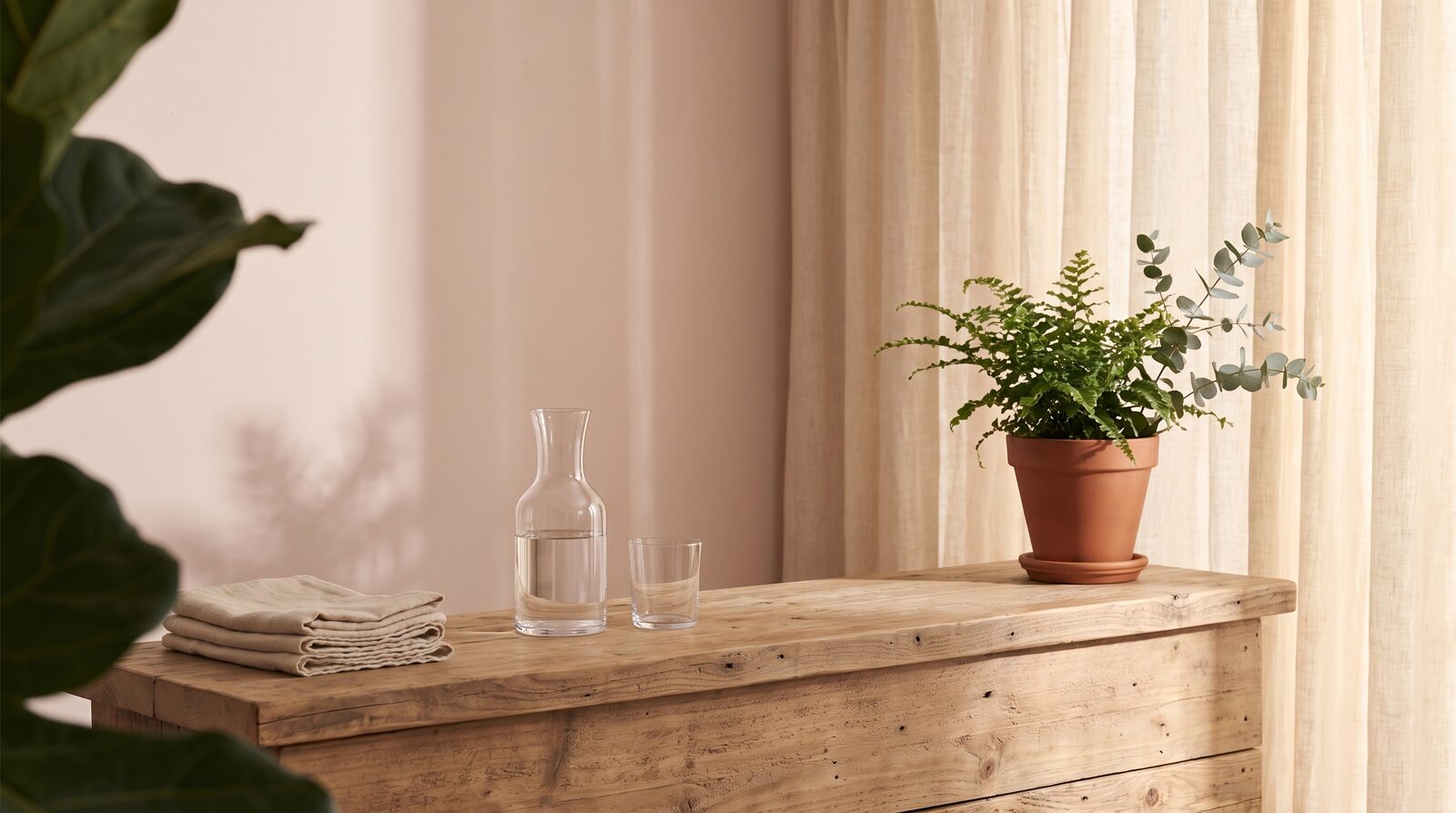 Fern & Soul massage studio in Innaloo, a timber console with a water carafe, folded cream linen towels and a potted fern.